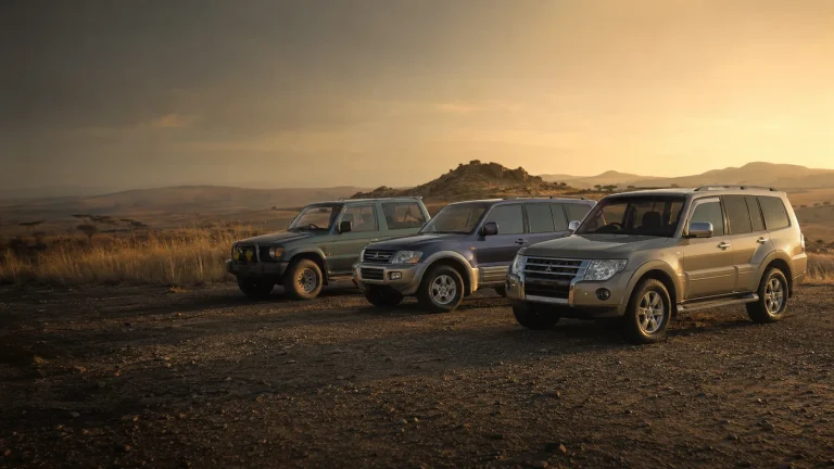 Three generations of Mitsubishi Pajero parked together on a gravel plain at golden hour in South Africa