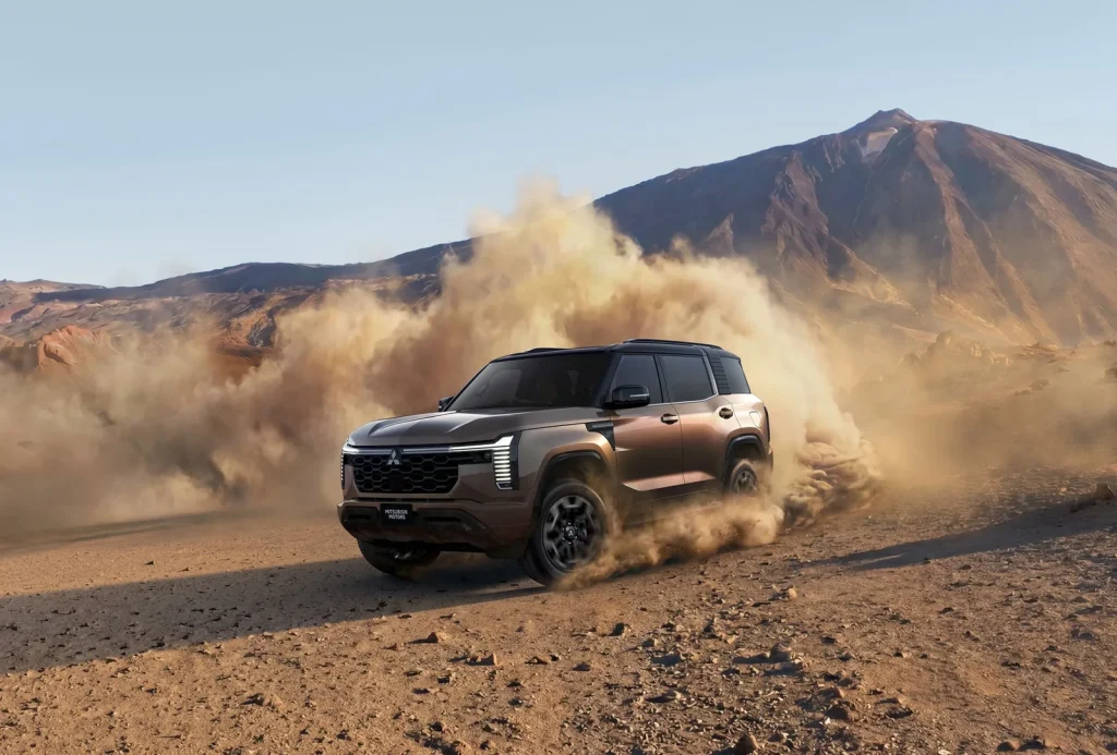 New Mitsubishi Pajero throwing up dust on a desert gravel road below a volcanic peak